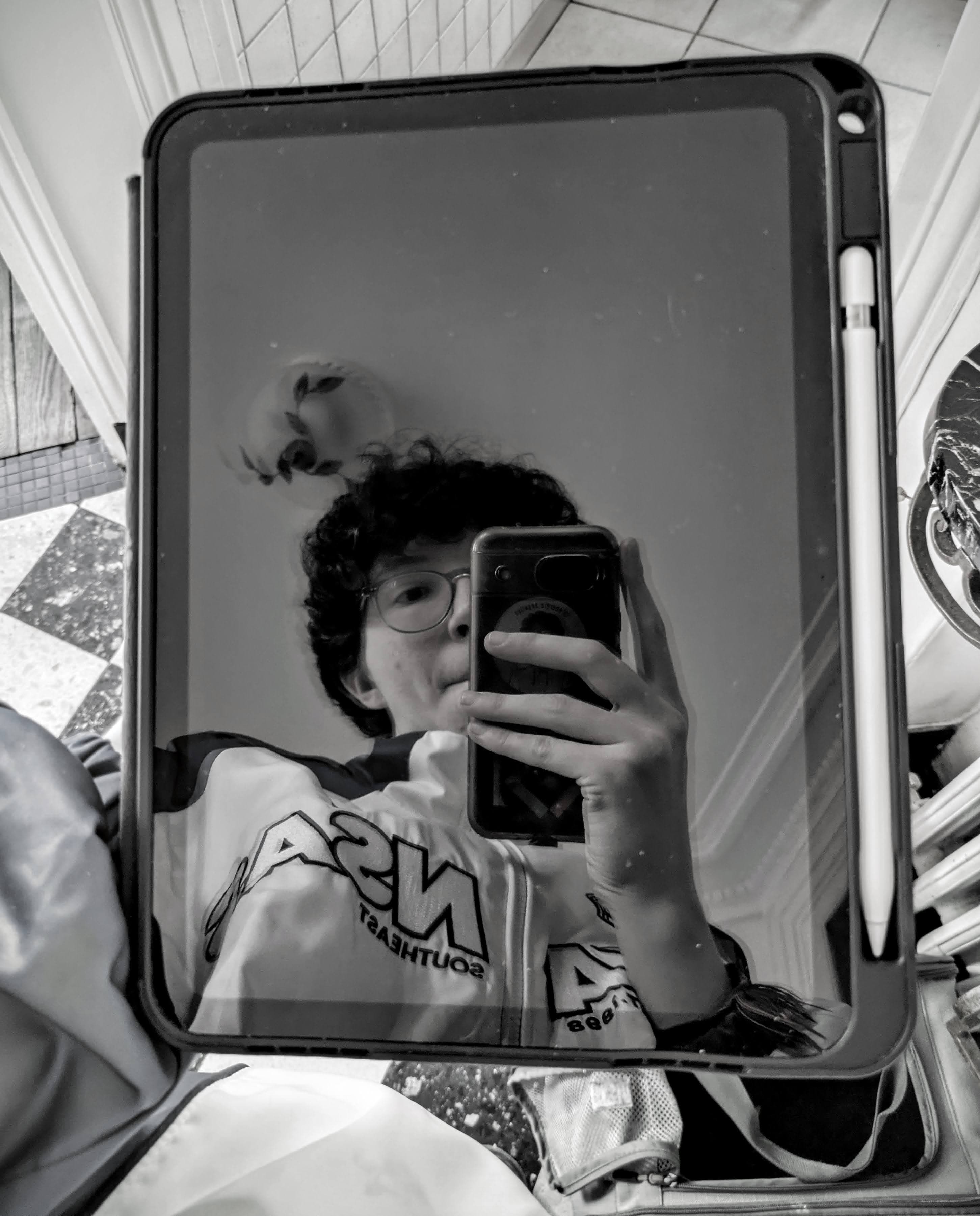 Selfie en noir et blanc dans le reflet d'un iPad, téléphone à la main, un Apple Pencil fixé sur le côté