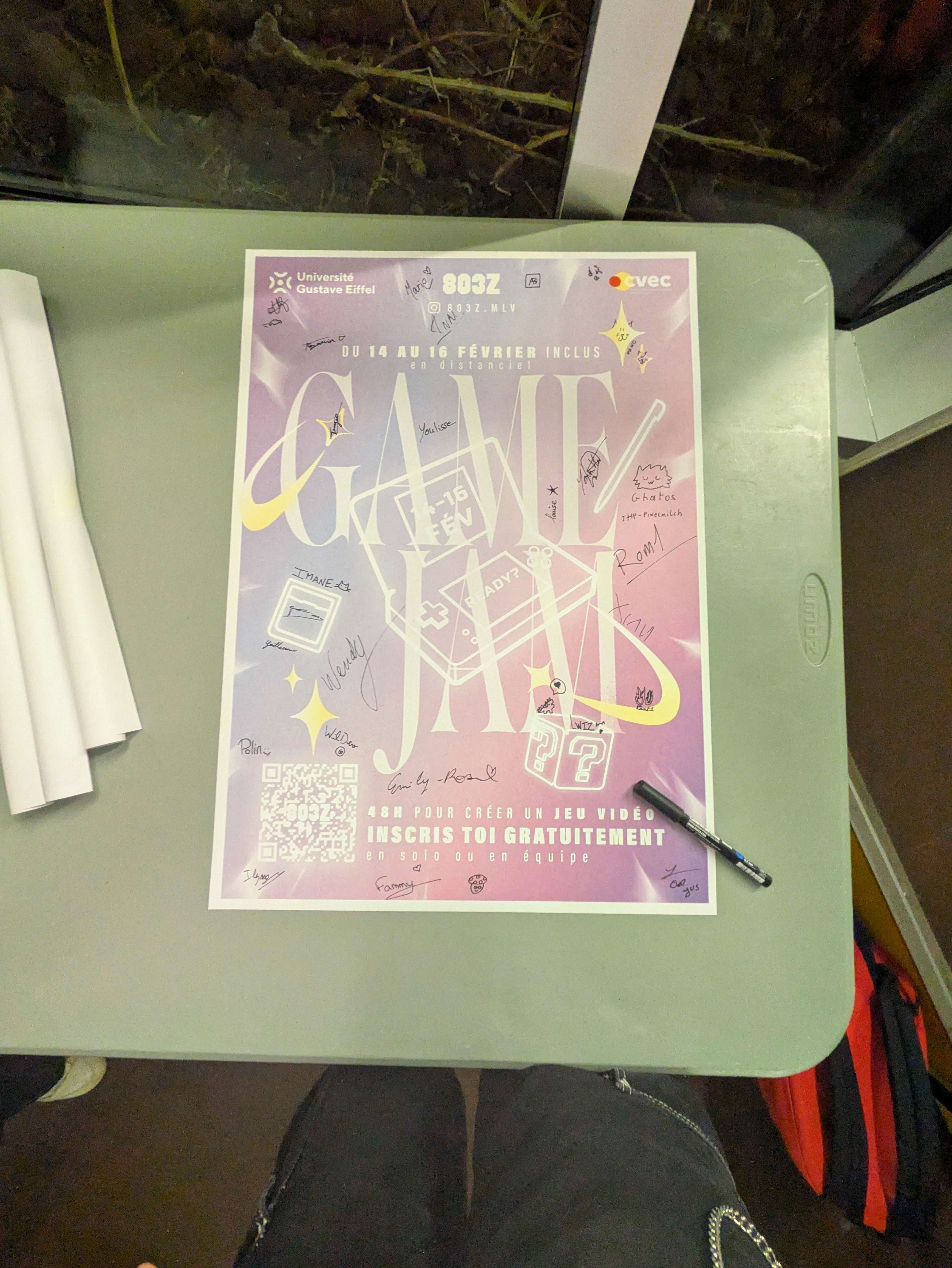 Une affiche imprimée de la Gamejam DS sur une table, à côté d'un stylo