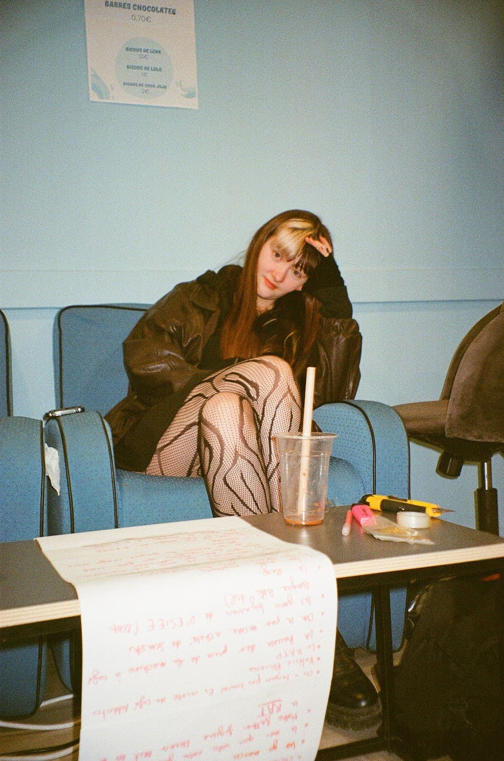 Louise accoudée dans un fauteuil bleu, derrière une table couverte d'un rouleau de papier manuscrit
